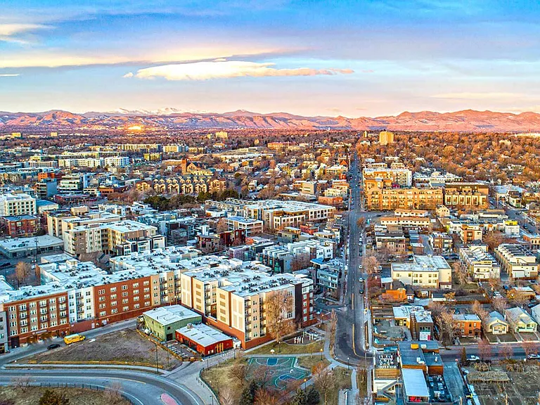 Breathtaking aerial view of a vibrant cityscape, showcasing a harmonious blend of urban architecture and scenic mountain backdrop at sunset.