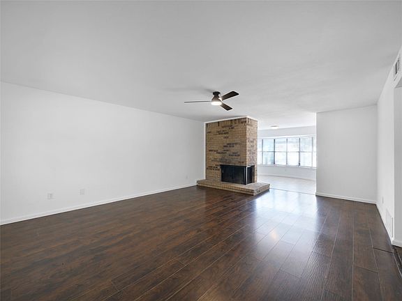 Expansive room featuring wood-finish flooring, a brick fireplace with hearth, and a ceiling fan