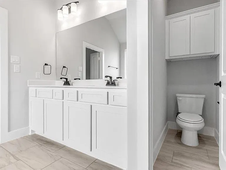 Bathroom featuring a dual vanity with white cabinetry, a large mirror, and matte black fixtures