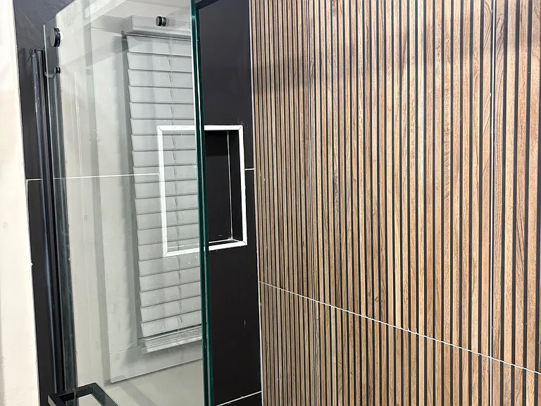 Glass-enclosed shower with built-in niche and hardware, paired with a slatted accent wall for added style.
