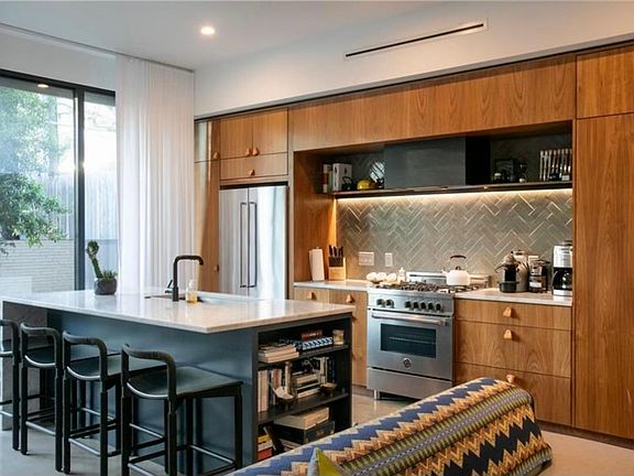 Open kitchen including custom kitchen backsplash, steel shelves/stove hood, and wood cabinets. Center island with big steel trough sink and quiet KitchenAid dishwasher. Bertazonni stove/oven and KitchenAid refrigerator/freezer.