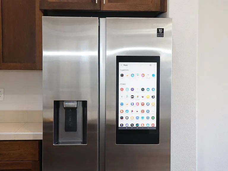 Sleek stainless steel smart refrigerator featuring a built-in touchscreen display with app integration, filtered water and ice dispenser, and smooth reflective surface
