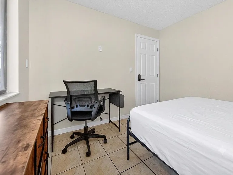 Bedroom features a furnished workspace, tiled flooring, and a large window for natural light and outdoor views.