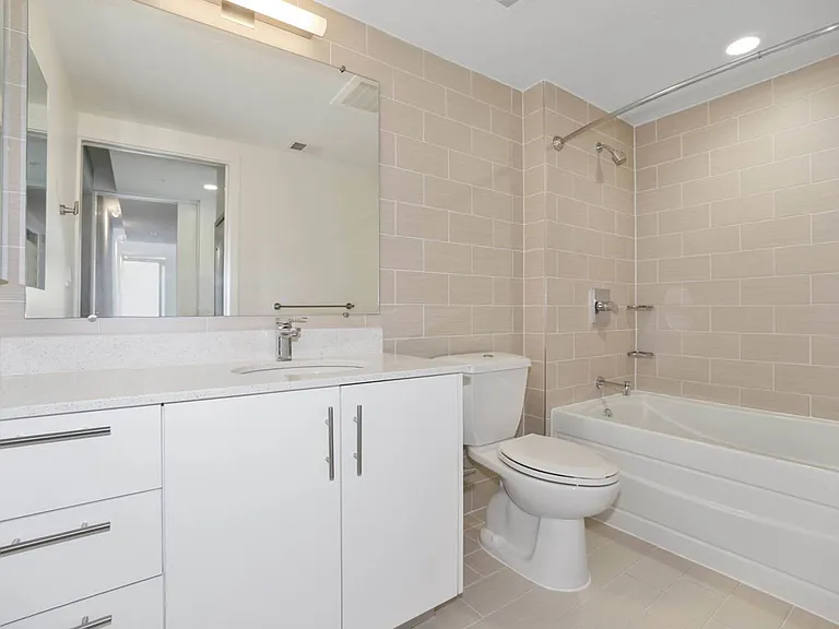 This sleek bathroom features a modern white vanity, expansive mirror, and a full-size soaking tub set against elegant beige subway tiles.