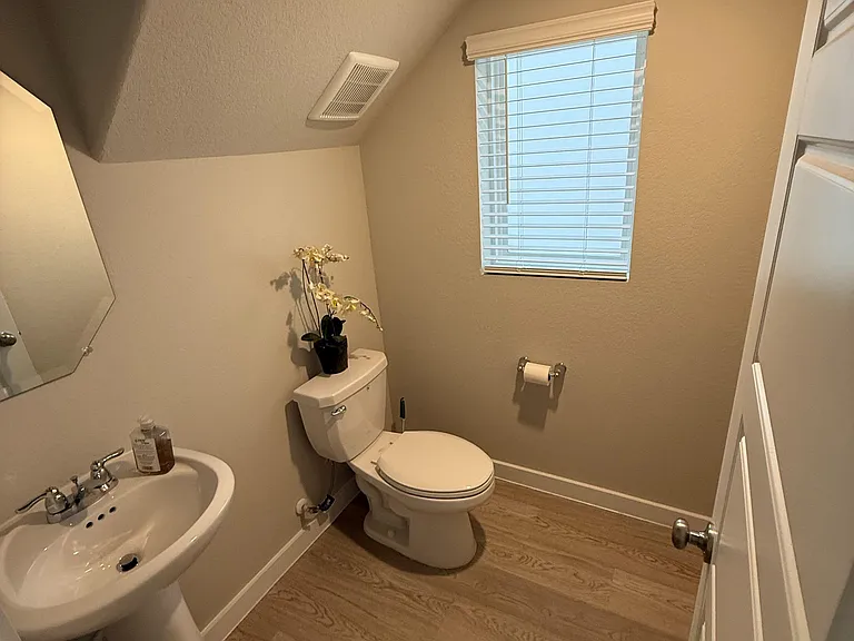 Half bath with pedestal sink, toilet, and wood-look flooring, plus a window with blinds for ventilation and privacy.