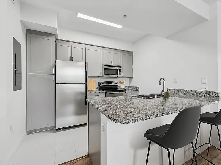 Renovated Package I kitchen with stainless steel appliances, tile backsplash, granite countertops (in most homes), and grey cabinetry