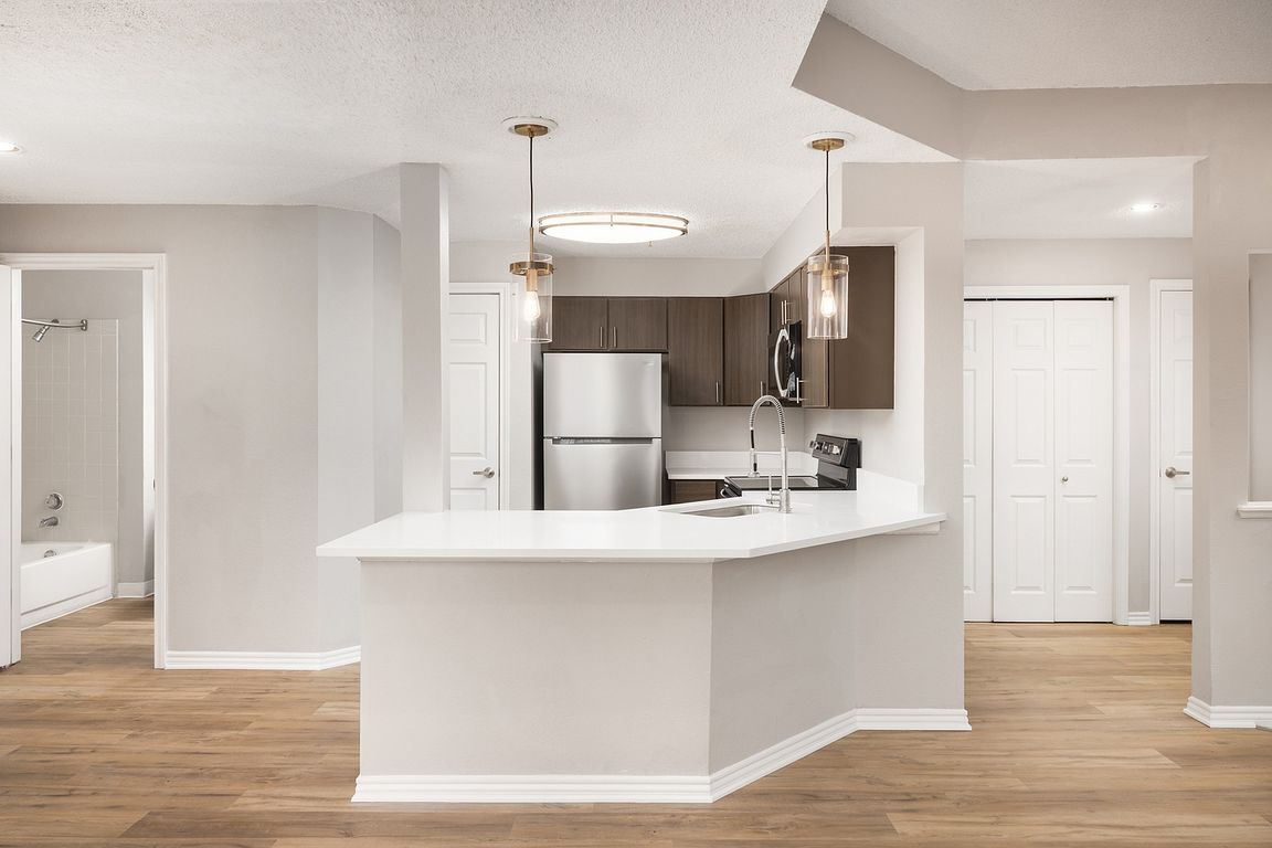 Modern apartment kitchen with elegant white countertops, stainless steel appliances, and warm wood flooring.