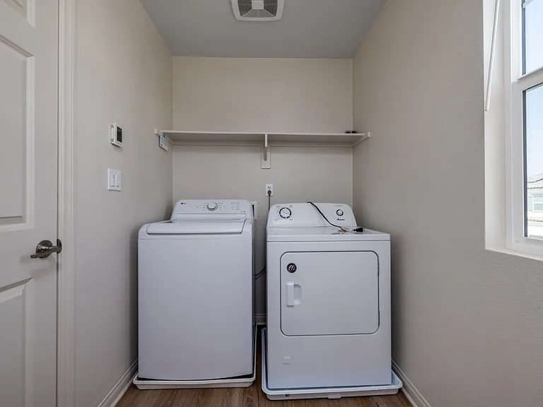 Upstairs laundry room with natural light, featuring a washer, dryer, and built-in shelving for easy organization and storage. Conveniently located near bedrooms for efficient daily living in this modern Menifee home.