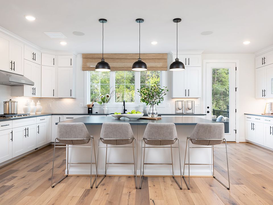 A modern, bright, and spacious kitchen with white cabinets, a large island with bar stools, and pend