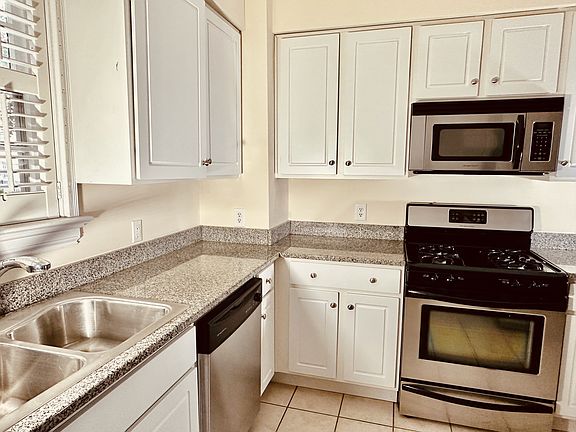 Bright kitchen with stainless steel appliances, granite countertops, gas range, built-in microwave, dishwasher, double sink, and ample cabinet space. Clean, modern design with tile flooring and plenty of natural light.