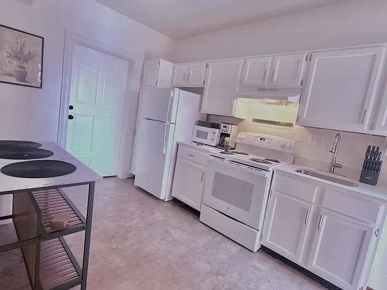 Galley kitchen with ample white cabinetry, full-size appliances, and a movable island for added prep and storage space.