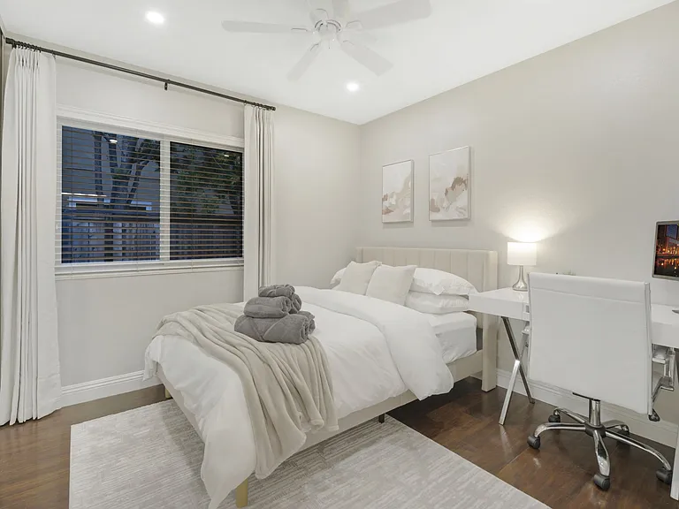 The bedroom features a cozy full-size bed with blackout curtains for restful sleep. A desk with a laptop monitor and an ergonomic office chair provides a perfect workspace. The spacious closet comes with hangers, offering ample storage.