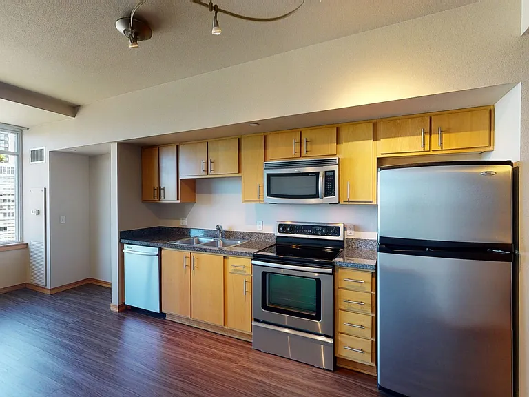 Apartment kitchen with stainless steel appliances, granite countertops and wood-style flooring.