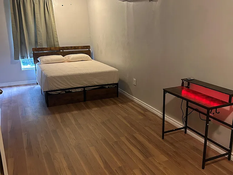 Spacious bedroom with wood-look floors, ceiling fan, window with curtains, and a mini-split A/C for year-round comfort.