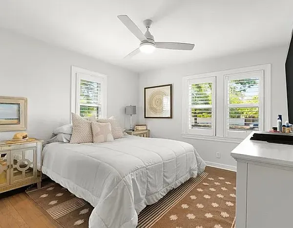 Primary bedroom with furniture (archival photo) with three windows with plantain shutters, hardwood floors, and large walk-in closet