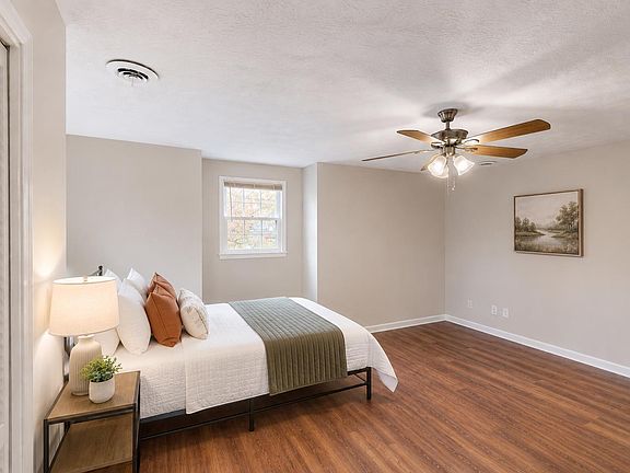 Spacious bedroom with wood-look floors, ceiling fan, and a large wall for storage; window brings in natural light.