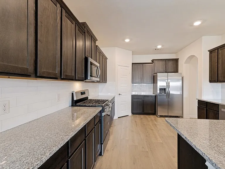 Kitchen featuring dark wood-finish cabinetry, light speckled countertops, stainless steel appliances, a white subway tile backsplash, and light wood-finish flooring
