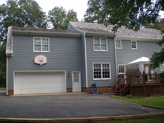 Back of home shows large parking pad, garage, basketball goal, & deck