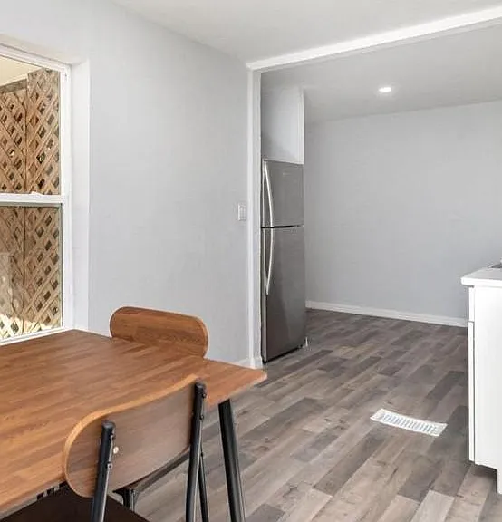 Open dining area flows into the kitchen with stainless refrigerator, durable plank-style flooring, and convenient layout.