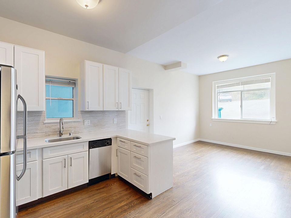 Bright kitchen with cabinets, stainless steel appliances, and wooden floors. A large window and a small island create an airy, modern feel.