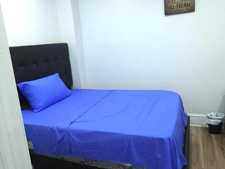 Compact private bedroom with a full bed, wood-look flooring, and space for a small nightstand or storage.