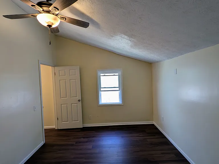 Bright and cozy back bedroom with fresh paint, sloped ceiling detail, and plenty of natural light from the window.