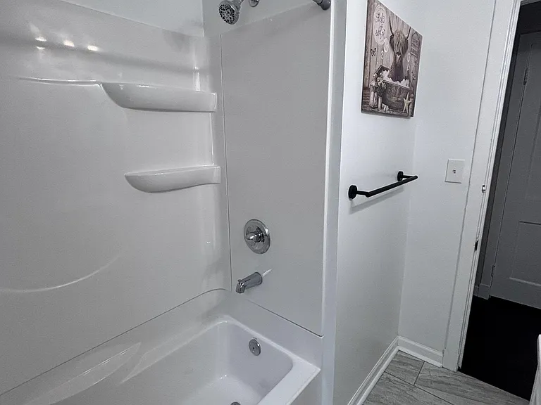 Clean full bath with tub/shower combo, built-in shelving, and tile-look flooring for easy everyday upkeep.