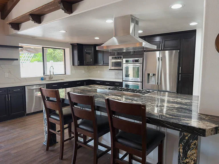 Chef-style kitchen with oversized stone island seating, dark cabinetry, and stainless appliances including double ovens.