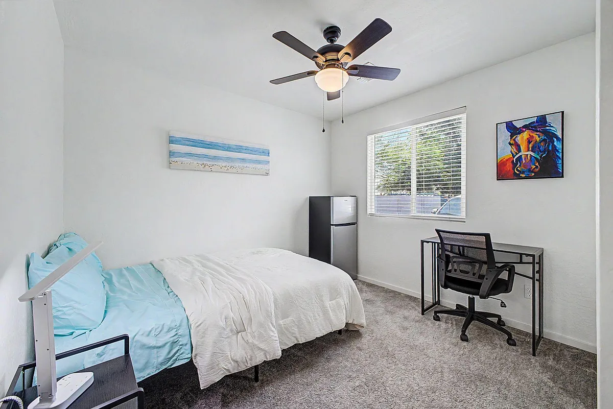 Photo 1 of 9 - W State Ave - Phoenix, AZ Furnished bedroom with a full bed, dedicated desk setup, ceiling fan, and a large window with blinds for natural light. - W State Ave