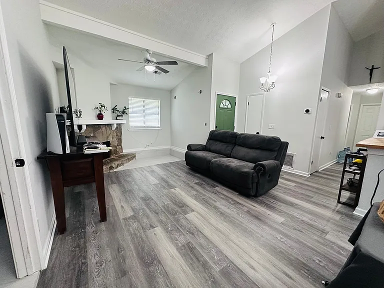 Step into a bright and inviting living space featuring soaring vaulted ceilings and a floor-to-ceiling stone fireplace that serves as the heart of the home. The spacious open-concept layout seamlessly connects the living room, dining area, and kitchen.