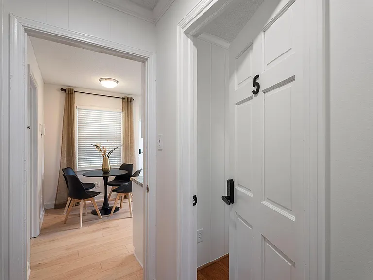 Compact dining nook with a round table for four, set beside a window with blinds and drapery for added privacy.