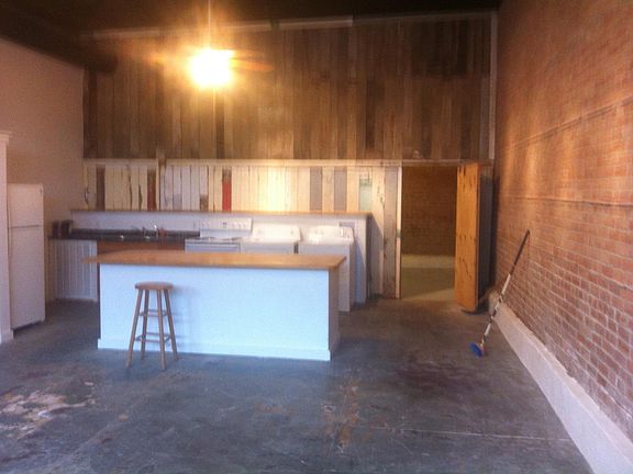Kitchen with island/ dining room area. Washer/dryer units next to oven. Door leads to back bedroom area and bathroom.