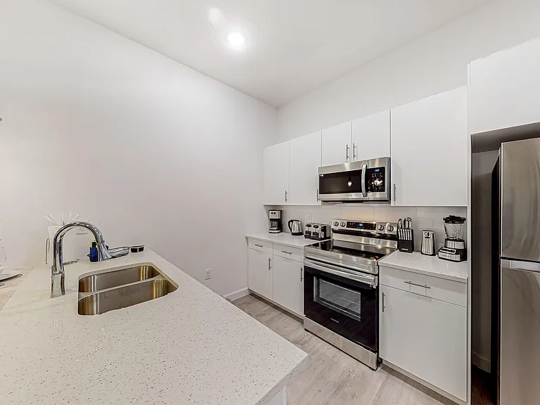 Open kitchen with quartz counters, double-basin sink, and stainless-steel appliance suite plus ample white cabinetry.
