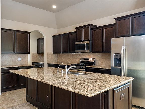 Large island in kitchen with granite countertops and beautiful dark wood cabinets including all stainless steel appliances.