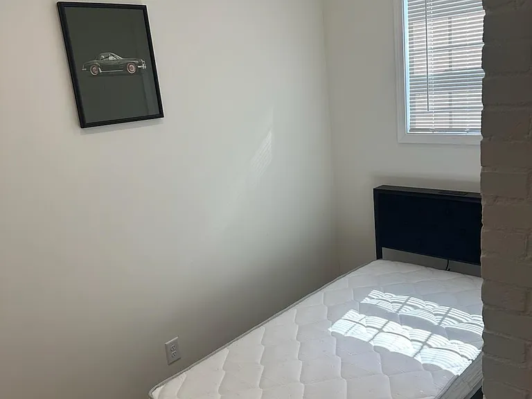 Private bedroom with a bed frame, hardwood-style flooring, and a window with blinds for light and privacy.