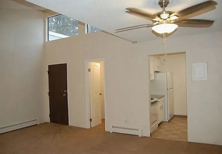Inviting apartment interior with a cozy kitchen, elegant ceiling fan, and abundant natural light from high windows.