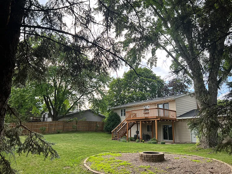 Fully fenced backyard with firepit, raised garden bed, perennial flowers, string lights, and large deck.