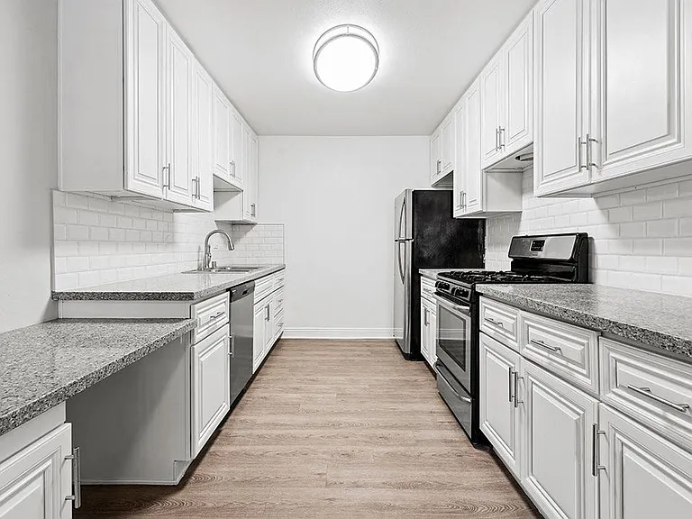 Large white tiled kitchen with stainless steel oven, microwave, and fridge.