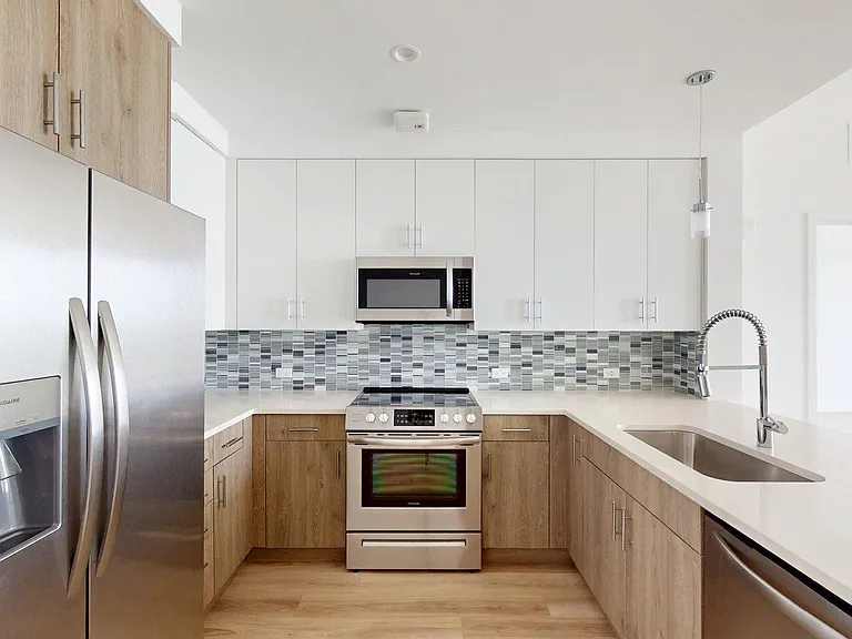 Apartment Kitchen with Stainless Steel Appliances, Quartz Countertops and Wood-Style Flooring.