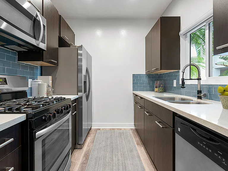 Blue tiled kitchen with granite countertop and stainless steel fridge, microwave, and fixtures.