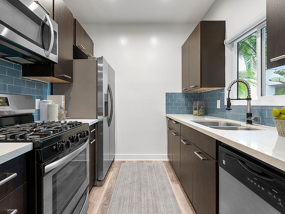 Blue tiled kitchen with granite countertop and stainless steel fridge, microwave, and fixtures.