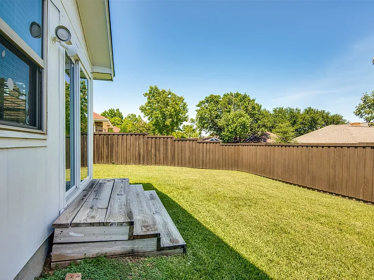 Spacious backyard featuring a wood privacy fence, a manicured lawn, and mature trees