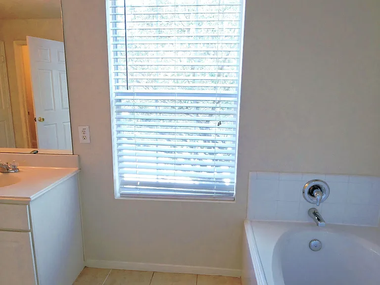 Full bathroom with tub/shower combo, wide vanity, and a large window with blinds for natural light and ventilation.