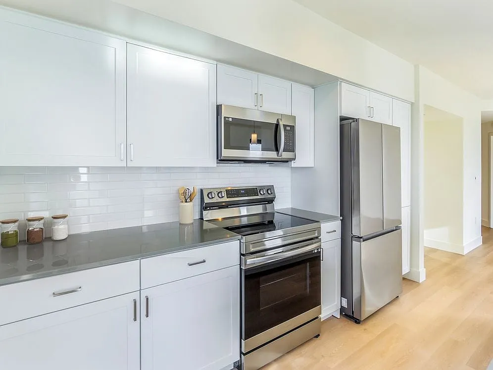 Renovated Package I kitchen with white cabinetry, grey quartz countertops, white subway tile backsplash, stainless steel appliances, and hard surface flooring - Avalon Towers Bellevue