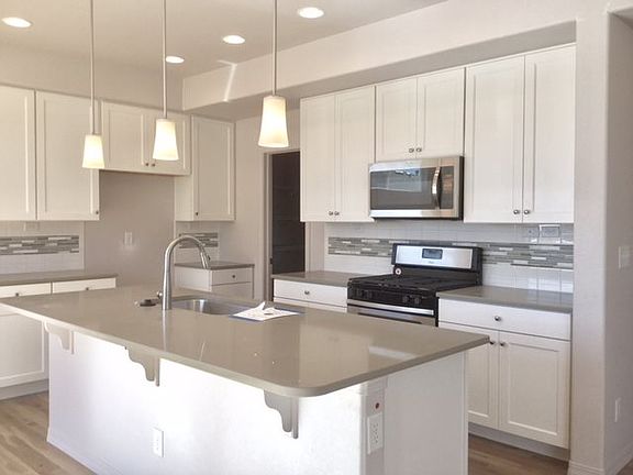 Beautiful kitchen with 42" white maple cabinetry, quartz counter tops, tile back splash, cabinet pulls, added can lighting, stainless steel appliance package and expanded hardwood flooring! (Photo of home under construction)