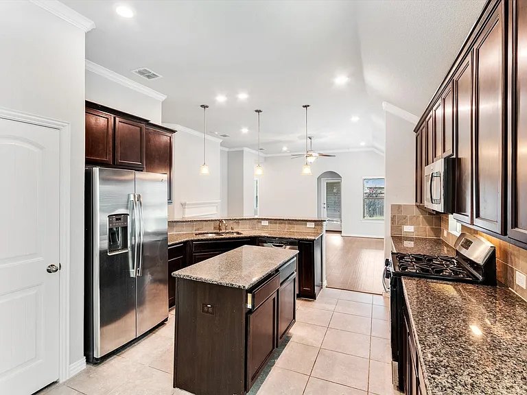 Kitchen featuring stone-finish countertops, wood-finish cabinetry, stainless steel appliances, a center island, and tile flooring