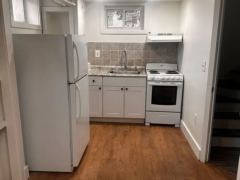 Efficient kitchen with full-size refrigerator, range, and sink, plus a tiled backsplash and durable flooring.