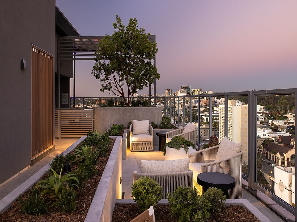 Chic rooftop terrace with cozy seating, lush planters, and stunning city skyline views at dusk.