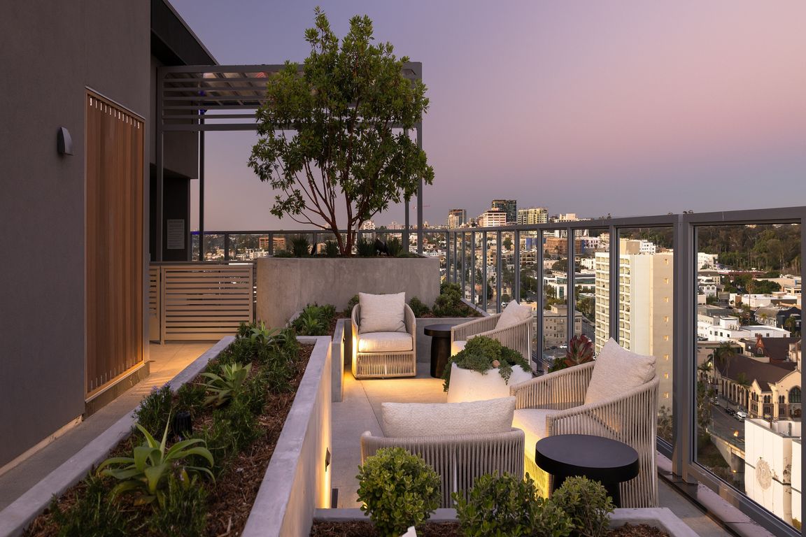 Chic rooftop terrace with cozy seating, lush planters, and stunning city skyline views at dusk.