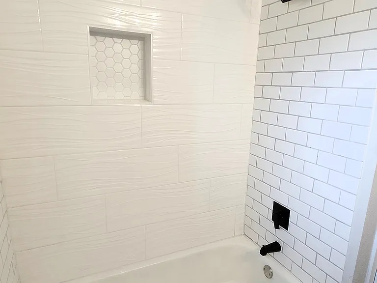 Elegant full bathroom design with enclosed tub offers white subway tiles, a modern black showerhead, enclosed niche, and stylish patterned floor tiles, creating a clean and contemporary look.